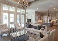 Lovely living room features a pair of ivory linen nailhead chairs facing a pair of ivory tufted chairs across from a rectangular mirrored coffee table alongside a white swoop arm sofa atop a blue trellis rug illuminated by an iron candelabra chandelier.